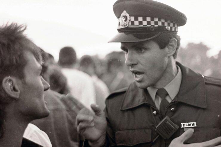 Una foto en blanco y negro. En primer plano, sobre el fondo de una muchedumbre, un Policía avisa un chico que no parece tomárselo muy en serio.