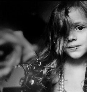 Foto blanco y negro retrato de un niña con una rosa en el fondo, obra de Letizia Battaglia.