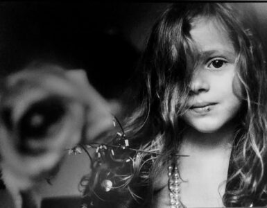 Foto blanco y negro retrato de un niña con una rosa en el fondo, obra de Letizia Battaglia.