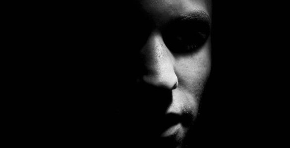 una cara sale de la oscuridad como si uN día ese Hombre se fue al Diablo. solo mitad del perfil se ve