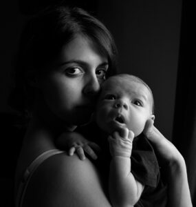 Una madre con un recién nacido en los brazos mira fijamente en la camara mientras el bebé parece absorto a los sonidos que lo rodean en un esfuerzo de aprender el lenguaje y el código de los sentidos