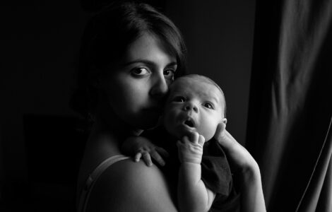Una madre con un recién nacido en los brazos mira fijamente en la camara mientras el bebé parece absorto a los sonidos que lo rodean en un esfuerzo de aprender el lenguaje y el código de los sentidos