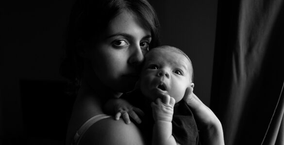 Una madre con un recién nacido en los brazos mira fijamente en la camara mientras el bebé parece absorto a los sonidos que lo rodean en un esfuerzo de aprender el lenguaje y el código de los sentidos