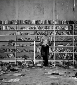 El protagonista de la foto es un lector en el medio de una habitación llenas de libros y medio en ruinas