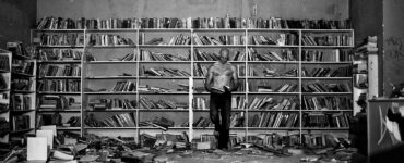El protagonista de la foto es un lector en el medio de una habitación llenas de libros y medio en ruinas